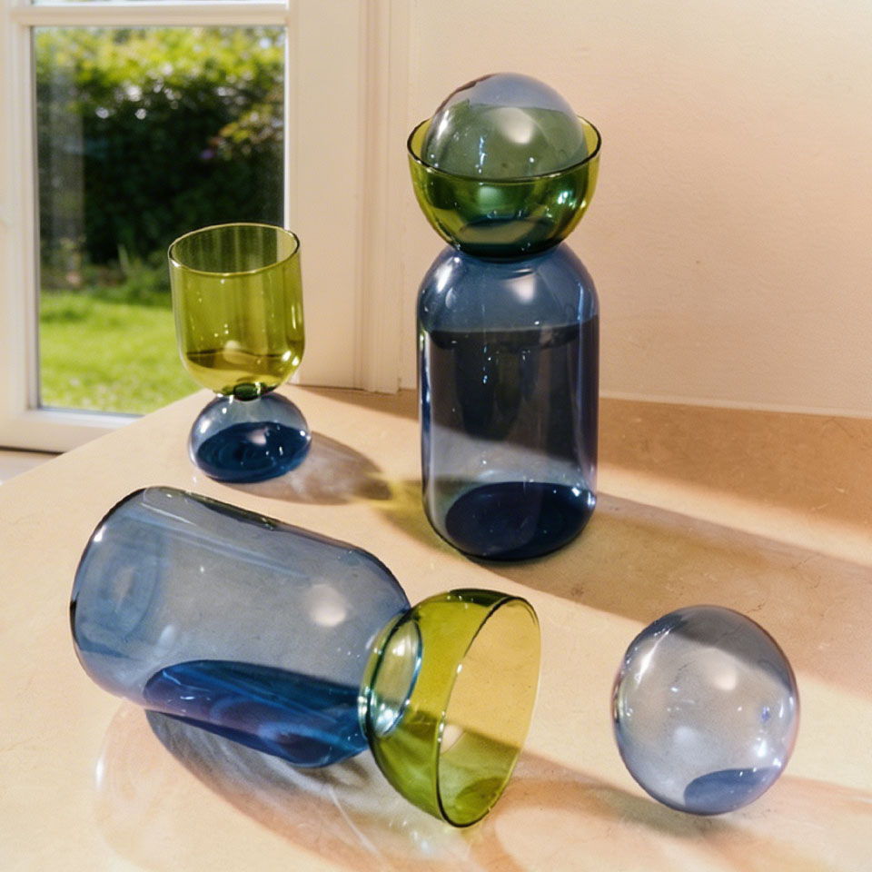 Colorful glass vases and a cup arranged on a surface with natural light.