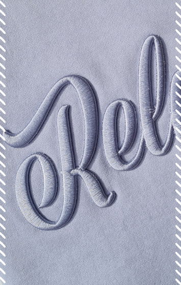 Close-up of tonal script logo embroidered onto powder blue fabric using raised with 3D puff embroidery stitching in matching powder blue thread