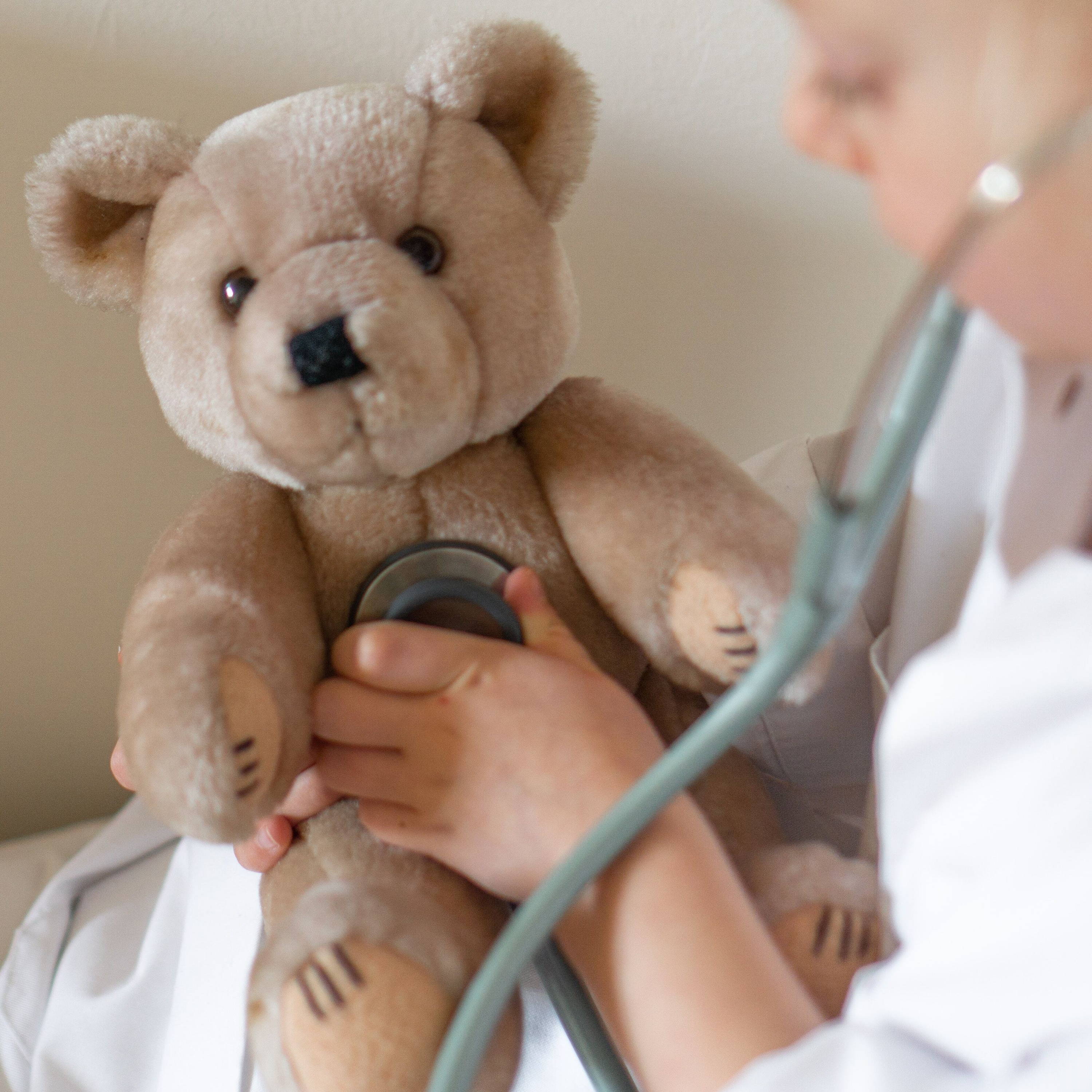 Enfant portant un manteau blanc jouant au médecin - il utilise un stéthoscope pour examiner son ourson en peluche