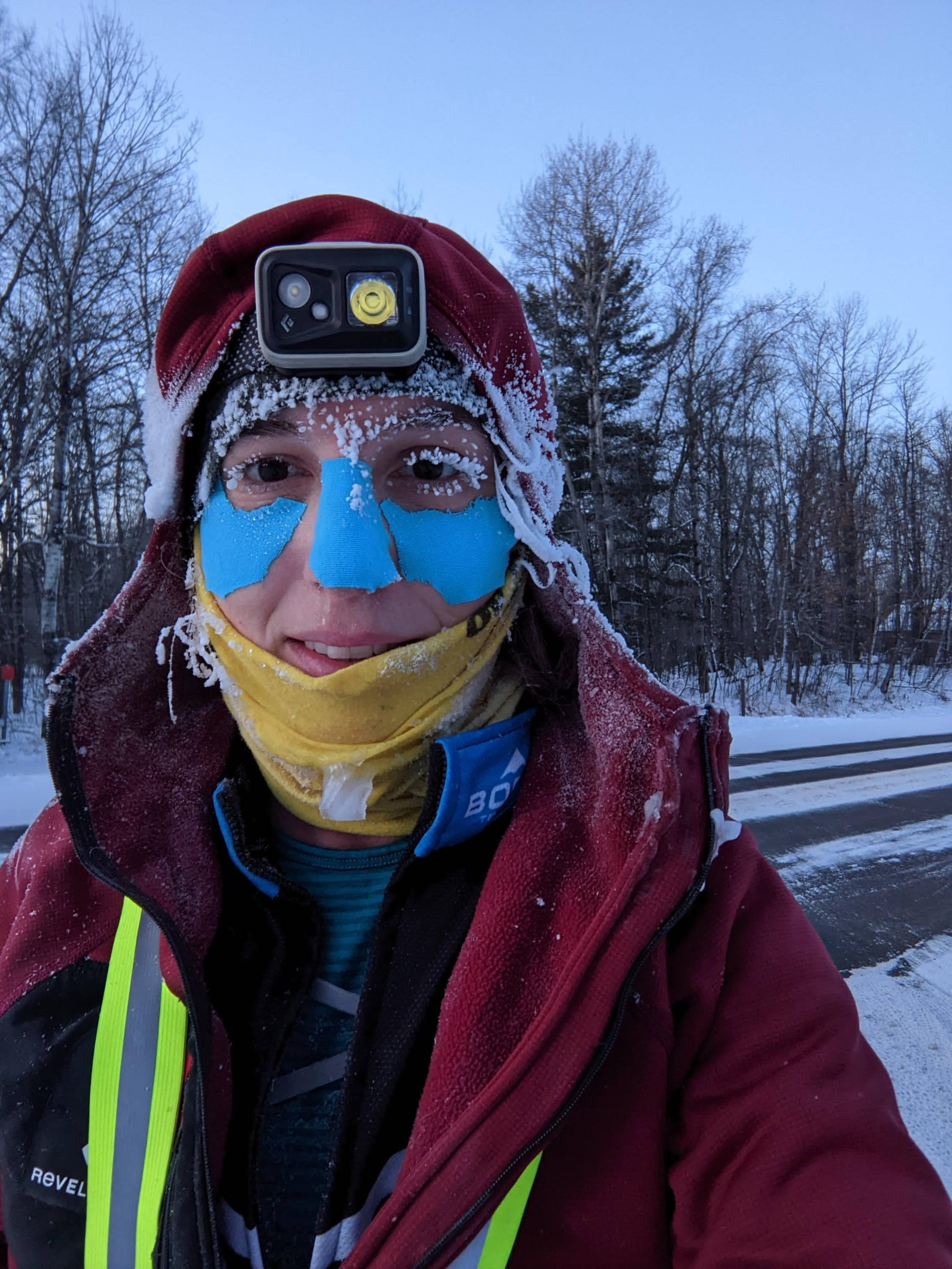 A woman with a headlamp and face protection shows off her frozen eyelashes.