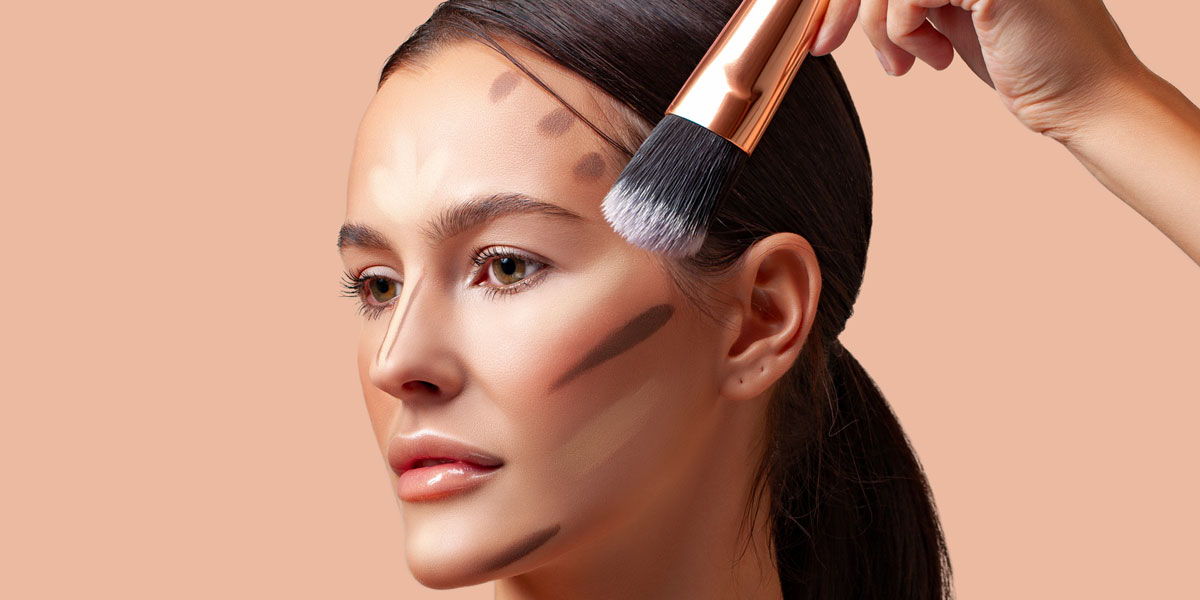 Woman applying makeup with a brush against a peach background.