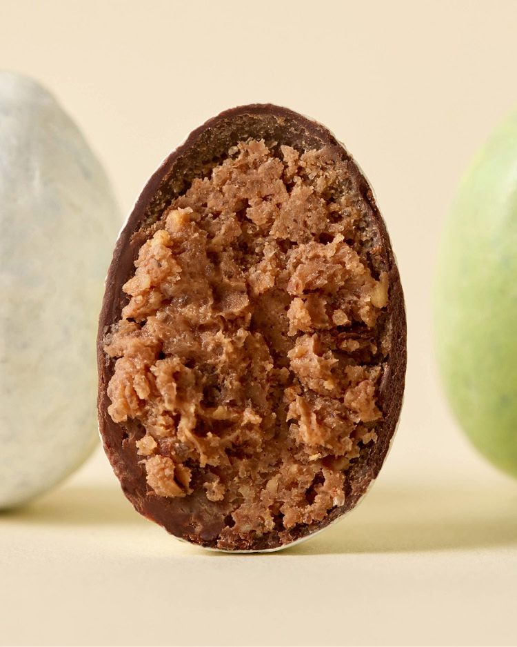 Chocolate egg cut in half, revealing a crunchy filling, with two whole eggs nearby.