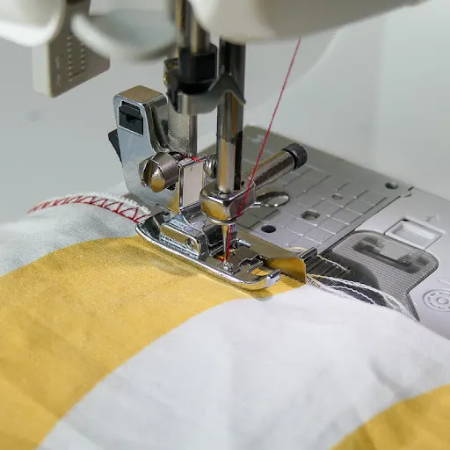Finishing edges with an overcast presser foot on yellow fabric, red overcast stitches