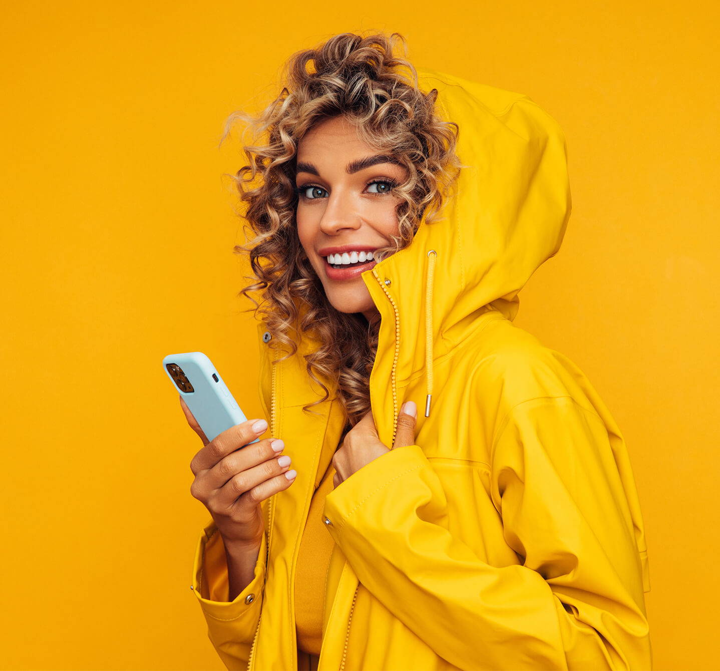 Wann ist Allergiesaison? Diese lächelnde Frau mit ihrem gelben Südwester verwendet den Kalender unserer App auf ihrem Handy.