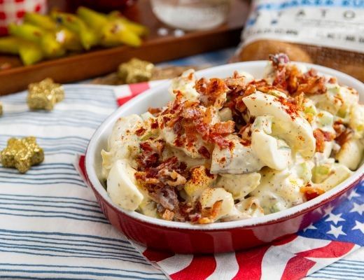 Bacon-topped macaroni salad in a dish on a patriotic tablecloth.