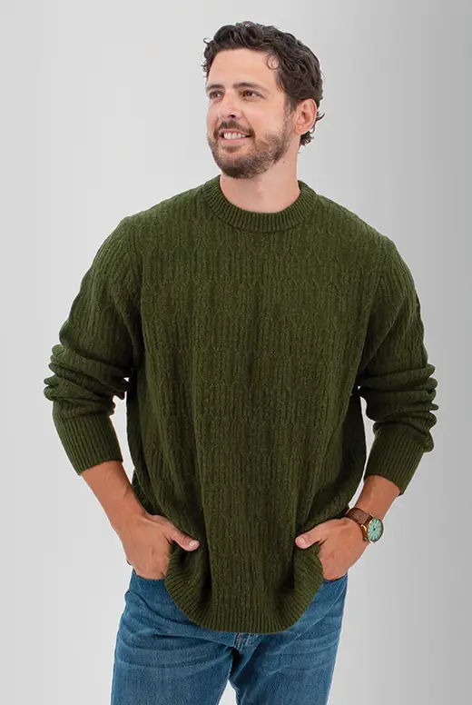 Man wearing a green sweater, smiling, with hands in pockets.