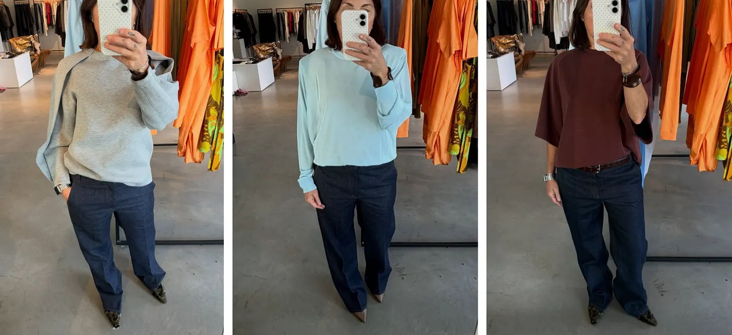 Person trying on three different colored sweaters in a clothing store.