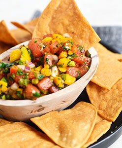Bowl of mango and watermelon salsa with tortilla chips on a black plate.