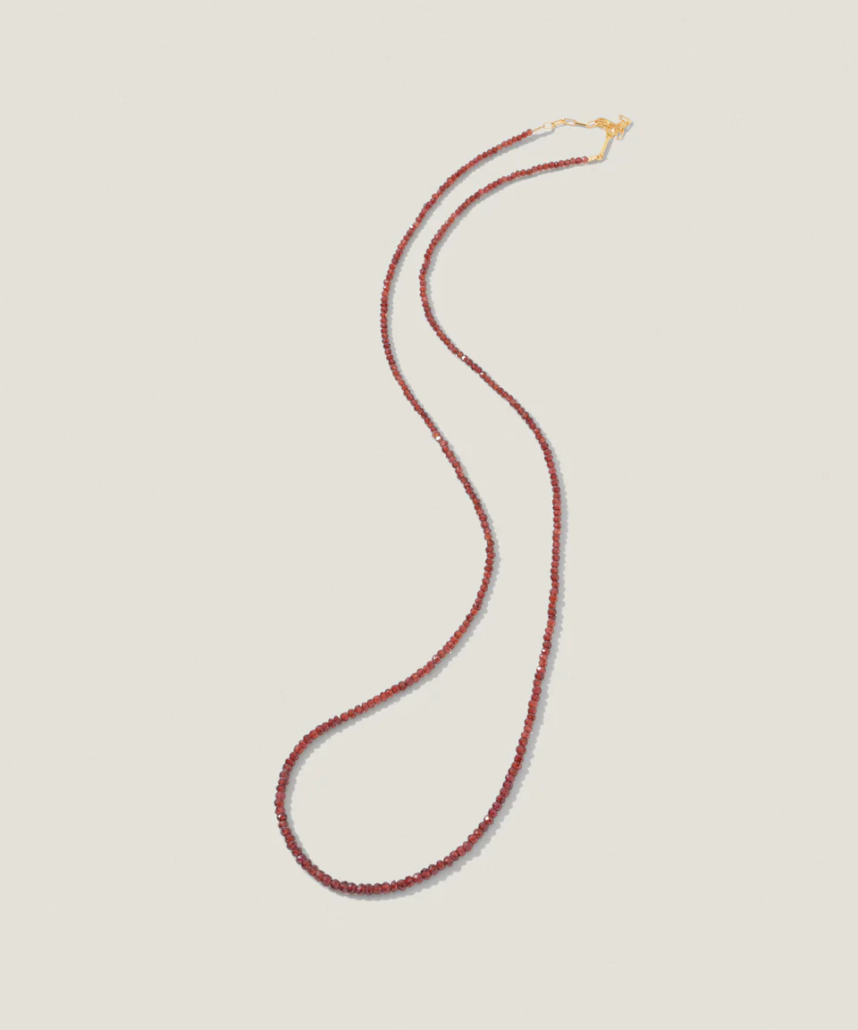 Red beaded necklace with a gold clasp on a neutral background.
