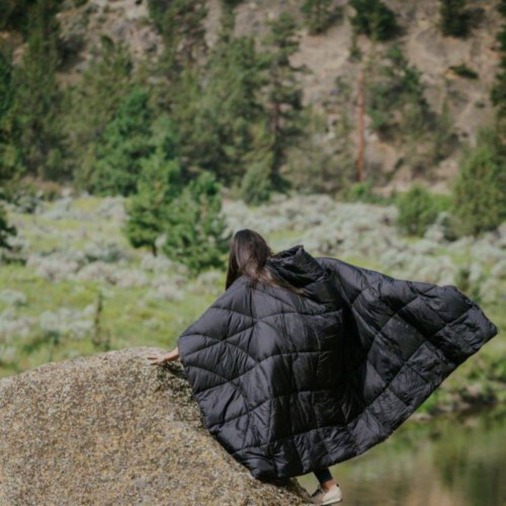 a person climbing a rock with a black Rumpl blanket around their shoulders
