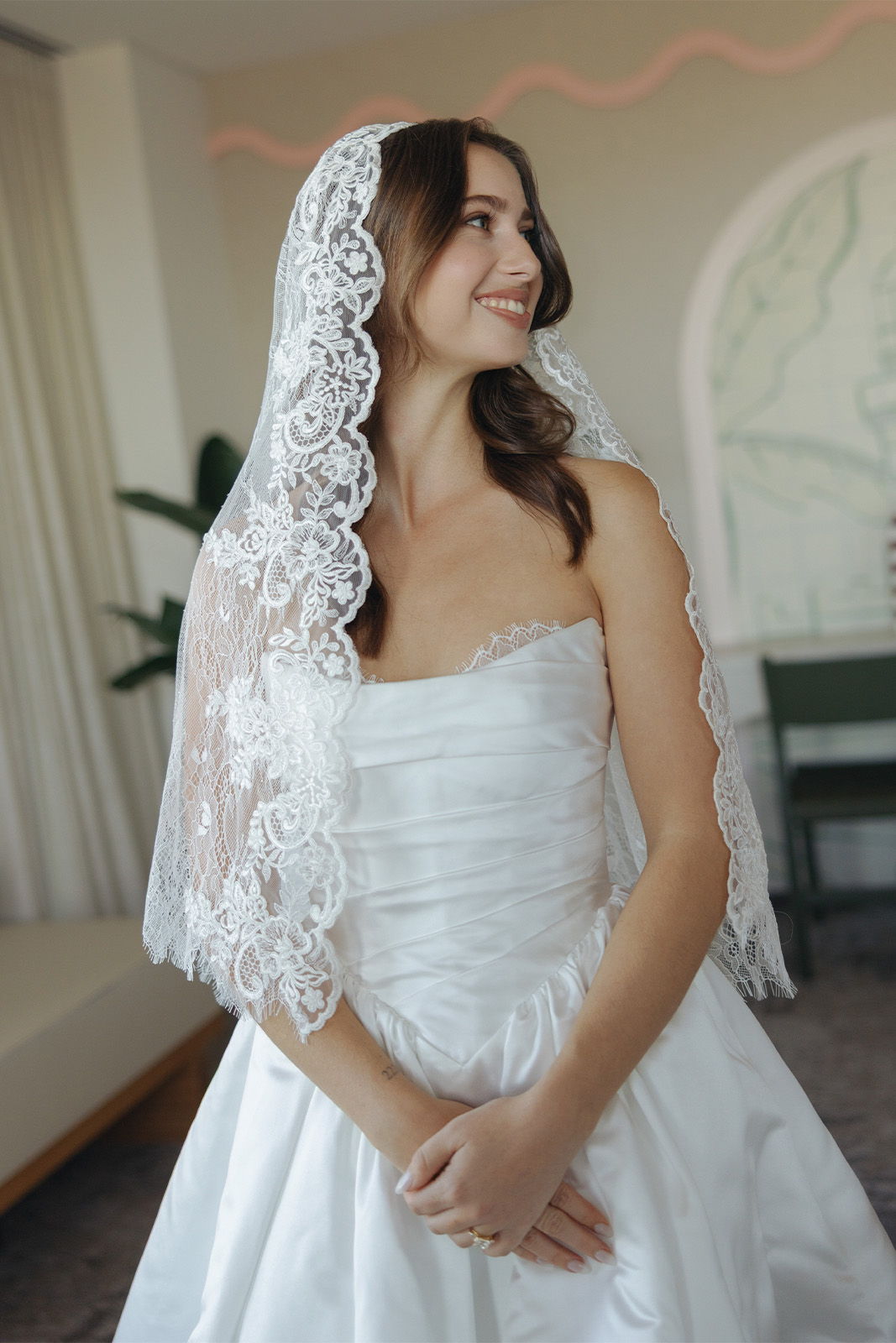 Bride in a white dress and lace veil, smiling softly.