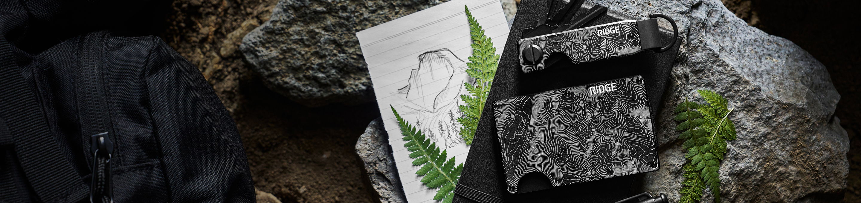 A flat lay of rocks, a black item, and a white package with greenery.