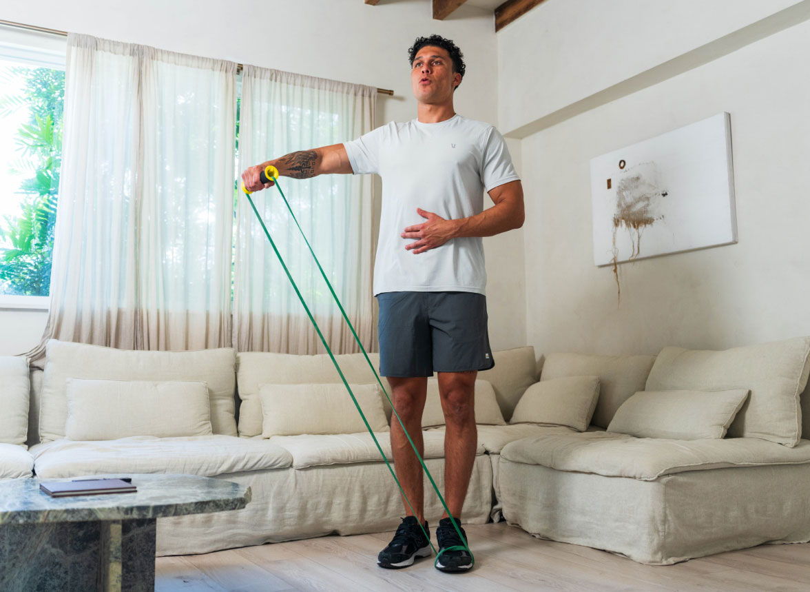 Man exercising with resistance band in a bright living room.