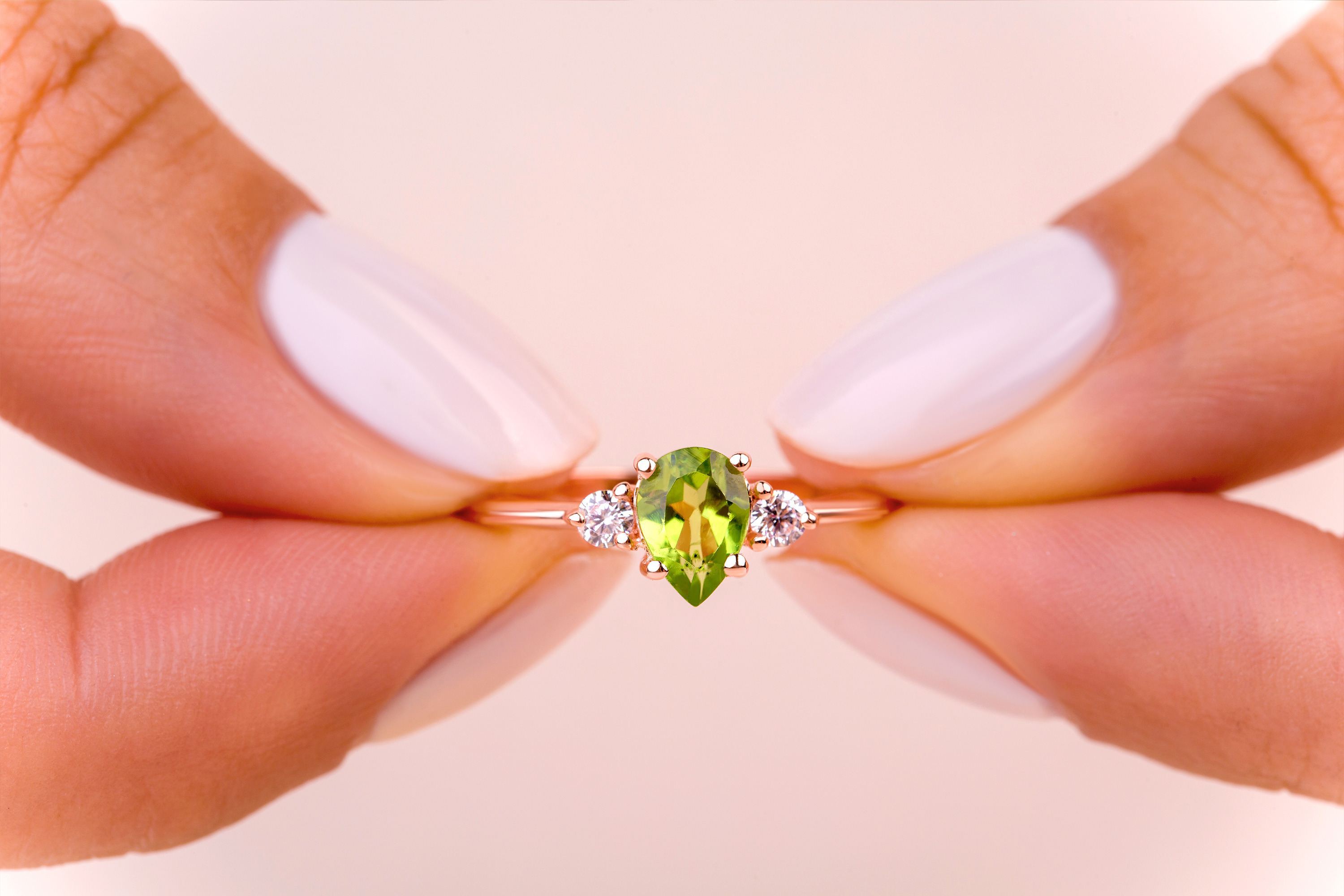 A woman is holding a Peridot gemstone ring in her fingers.