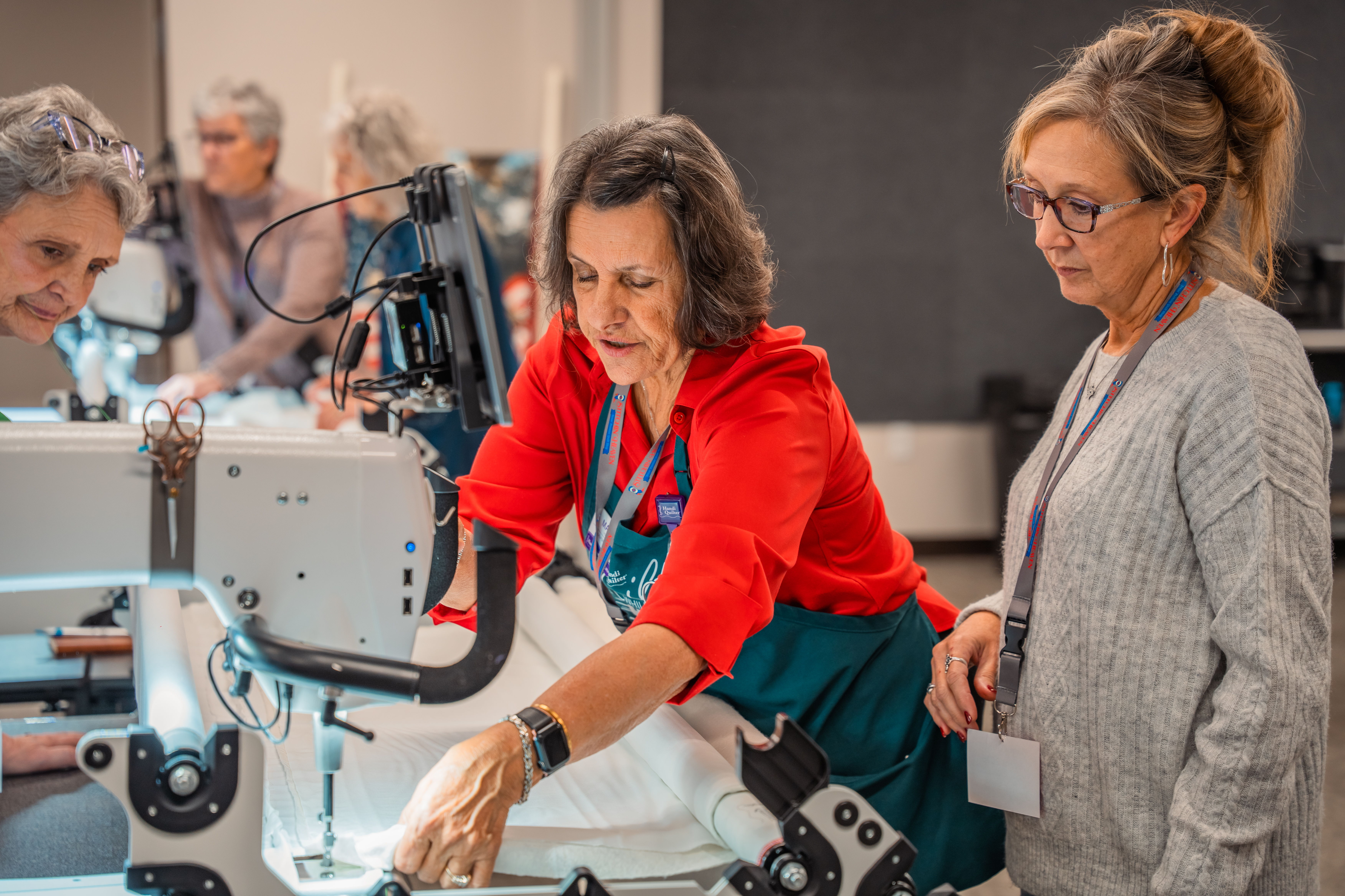 Group of people sewing with machines, focused on a woman in red shirt.