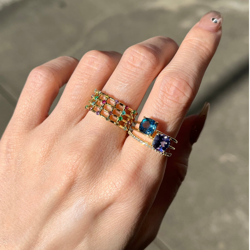 A hand wearing multiple colorful rings on a sunny day.