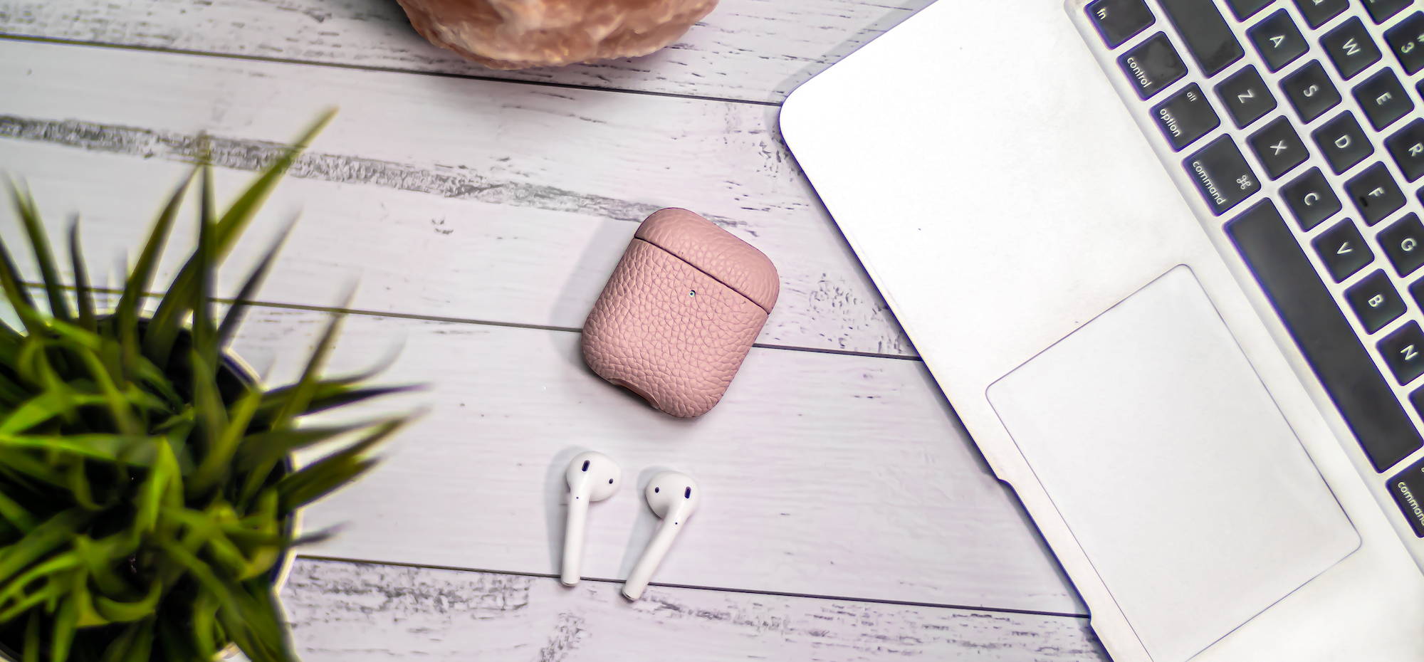 pink genuine leather airpods case laying flat on wooden table top with a silver macbook air
