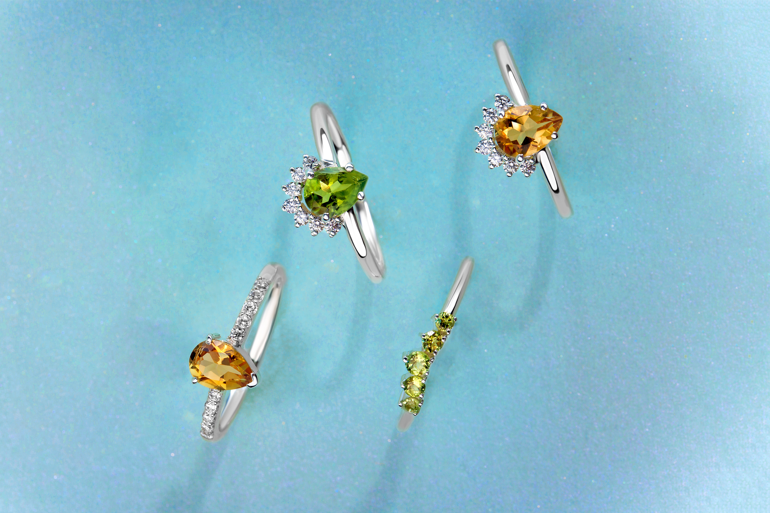 Two rings with Citrine gemstones and two rings with Peridot gemstones are presented on a blue surface.