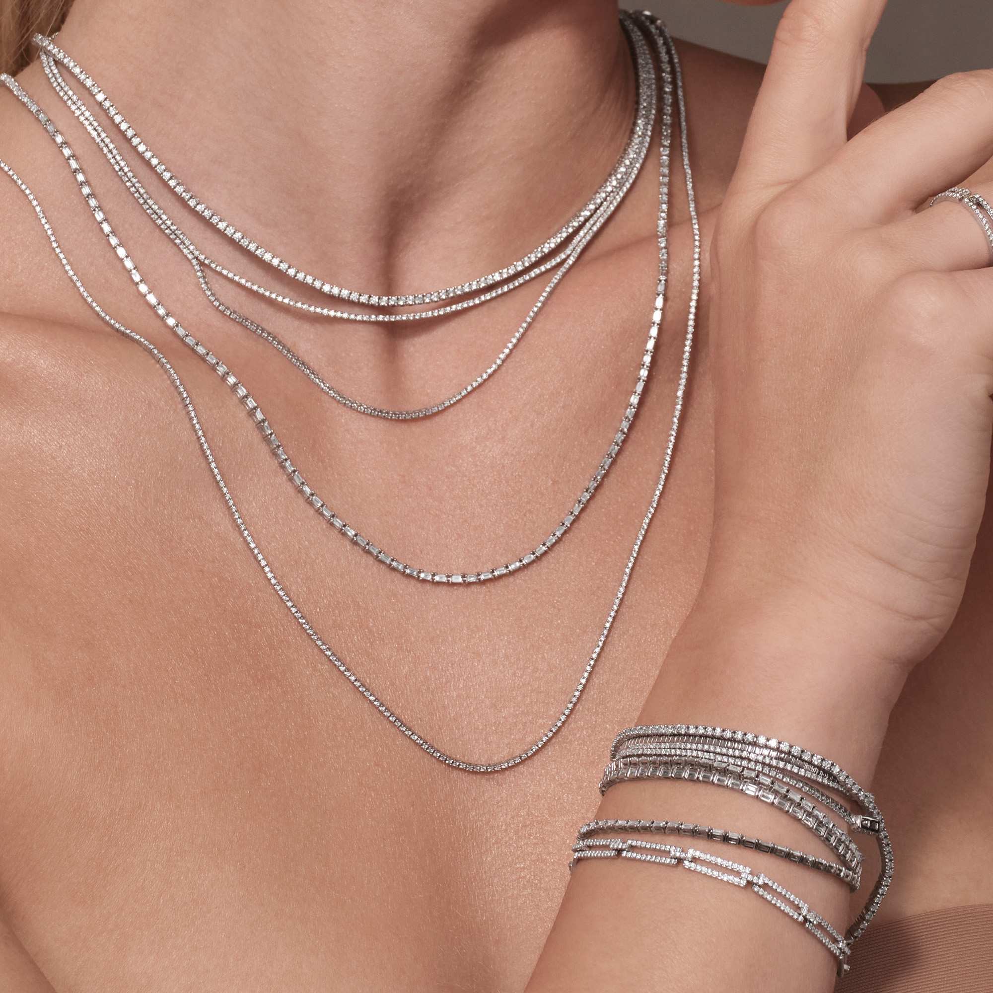 Close-up of layered silver necklaces and bracelets on a model's skin.