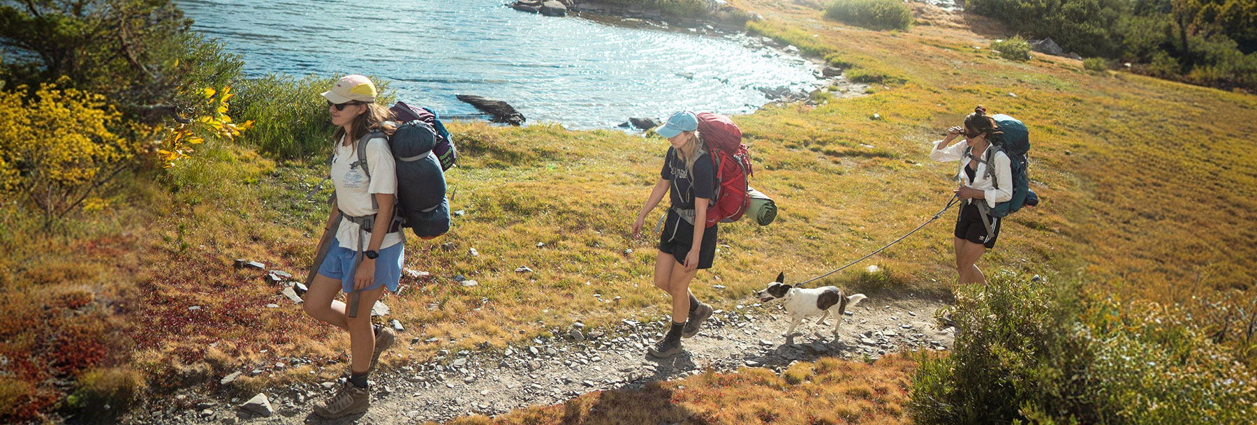 Three hikers walking along a trail near a scenic body of water.