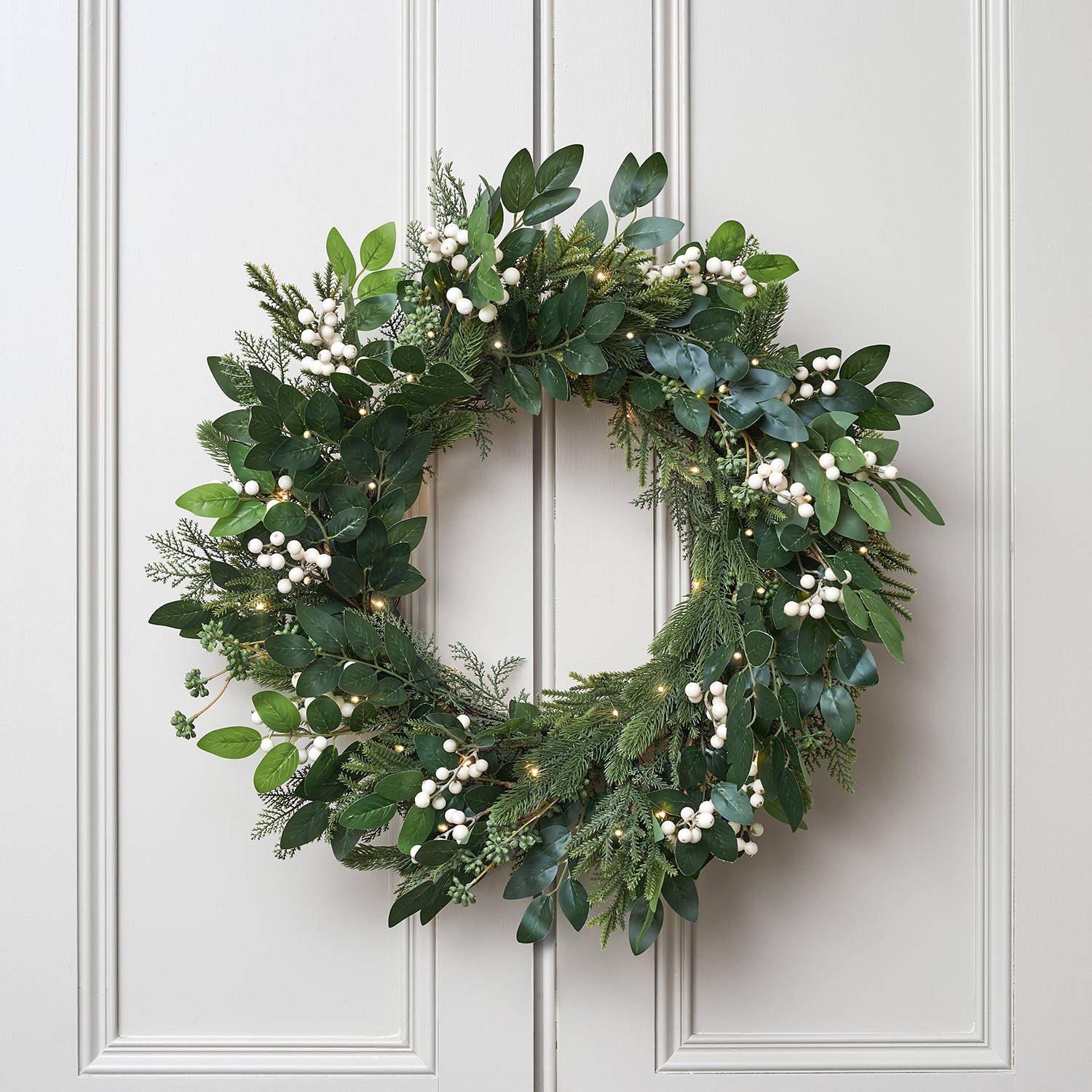Artificial wreath with lights on a white door with white berries.