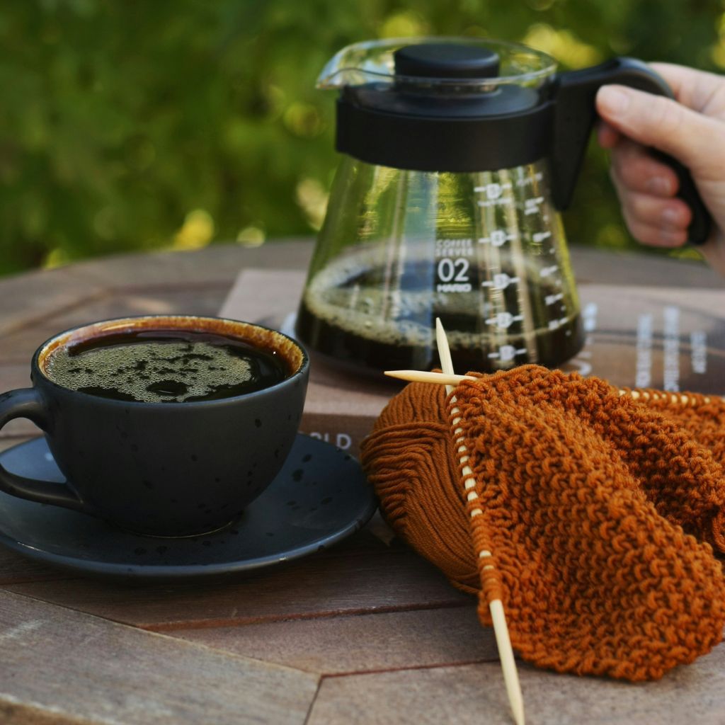 Eine Kaffeetasse und Kanne sowie ein Strickprojekt, das auf einem Holztisch liegt.