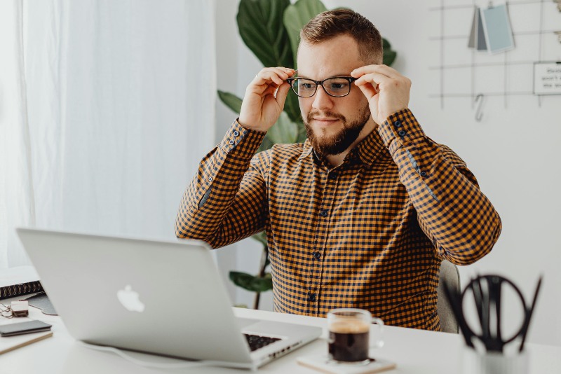 man putting on blue light glasses while working indoors on laptop