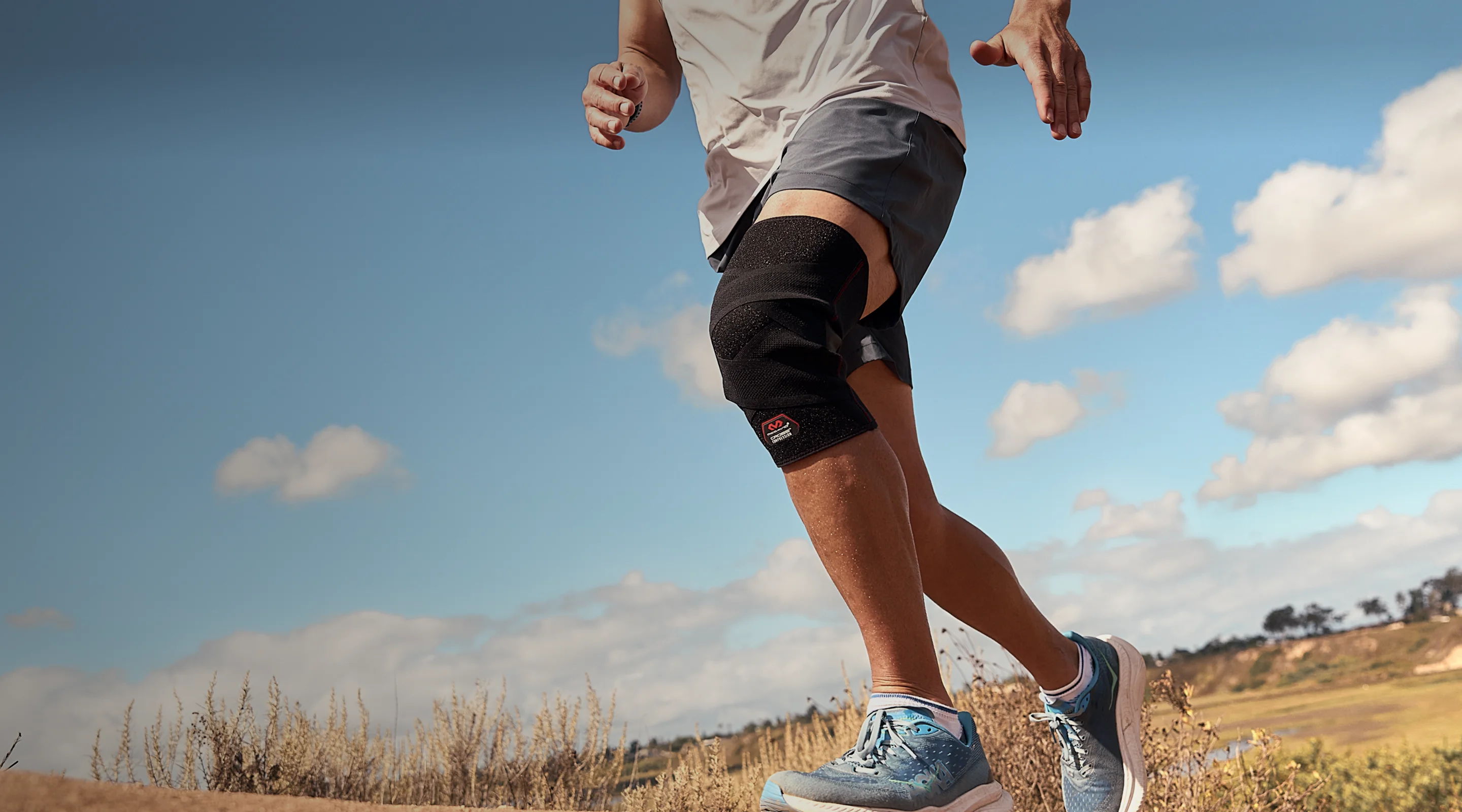 Person jogging outdoors wearing a knee brace and athletic clothing.