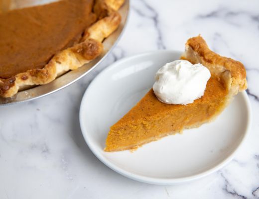 Slice of pumpkin pie with whipped cream on a white plate.