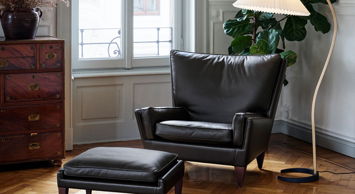 A cozy living room with a black V11 Lounge Chair by Gubi ottoman, and floor lamp.