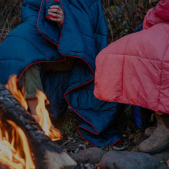 Couple sitting around the fire wrapped in Rumpl down blankets