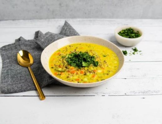 A bowl of soup garnished with herbs and a golden spoon.