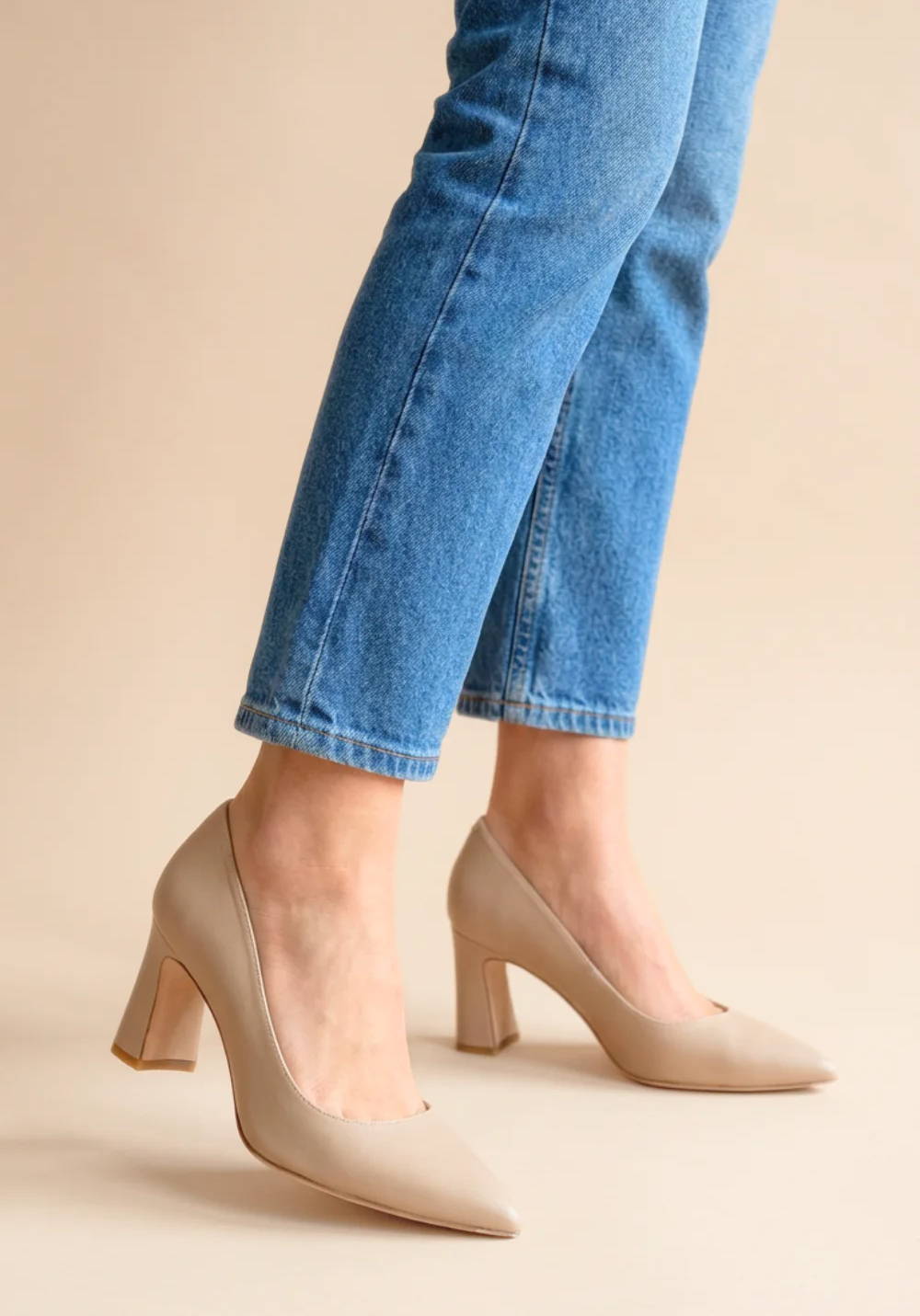 A person wearing beige high heel shoes and blue jeans.