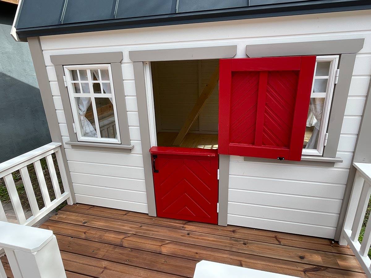 Kids Playhouse in white color with red dutch door and wooden terrace in a backyard by WholeWoodPlayhouses