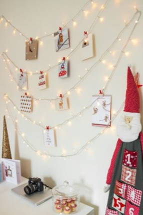 Fairy lights hung on a neutral wall  with Christmas cards attached and Christmas decorations around them.