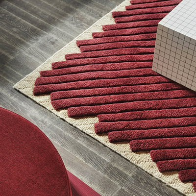 Red textured rug on wooden floor with a white geometric object.