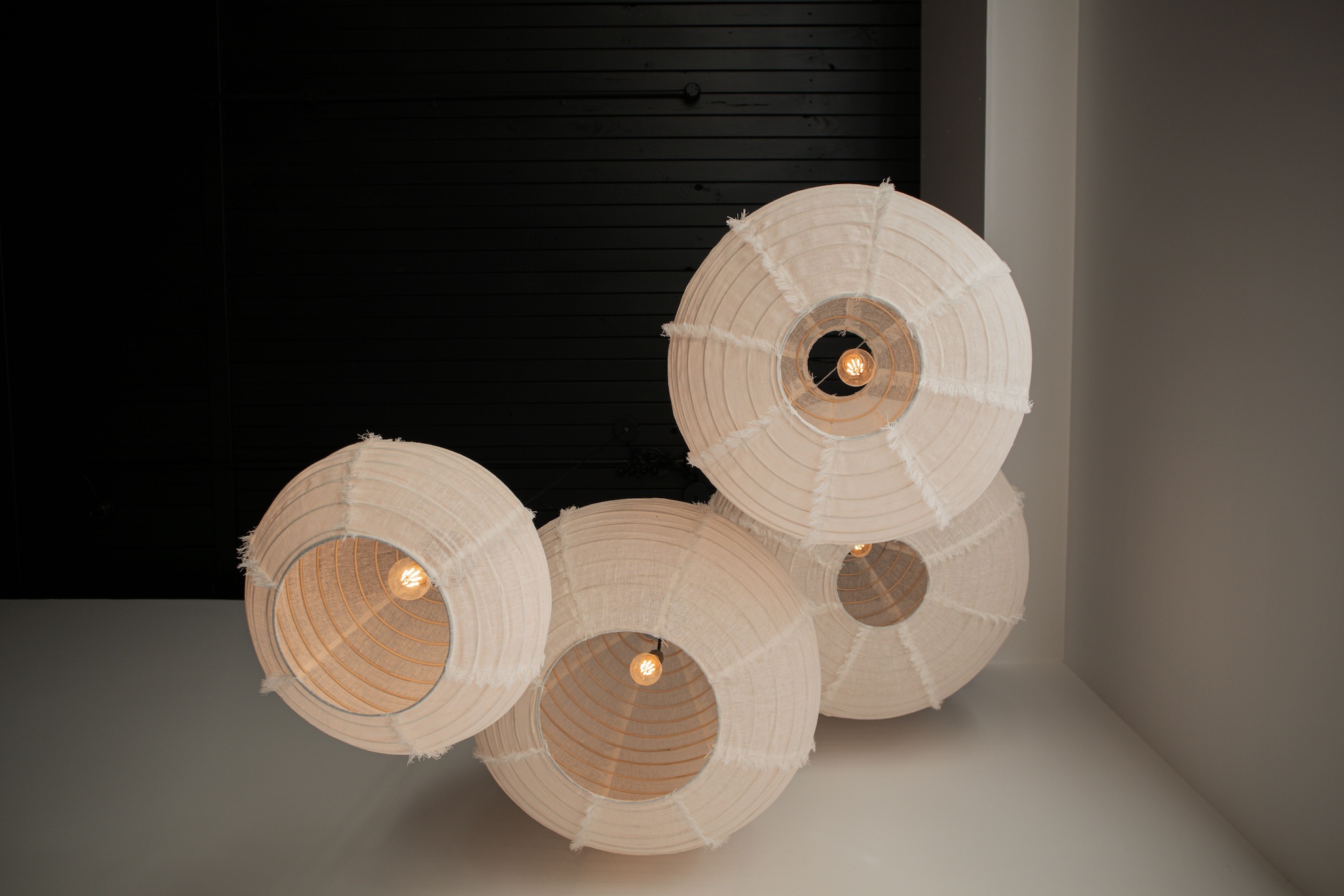 Four stylish white linen lanterns with warm light, arranged in a cluster
