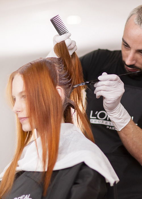 Hair stylist coloring long red hair on a female client.