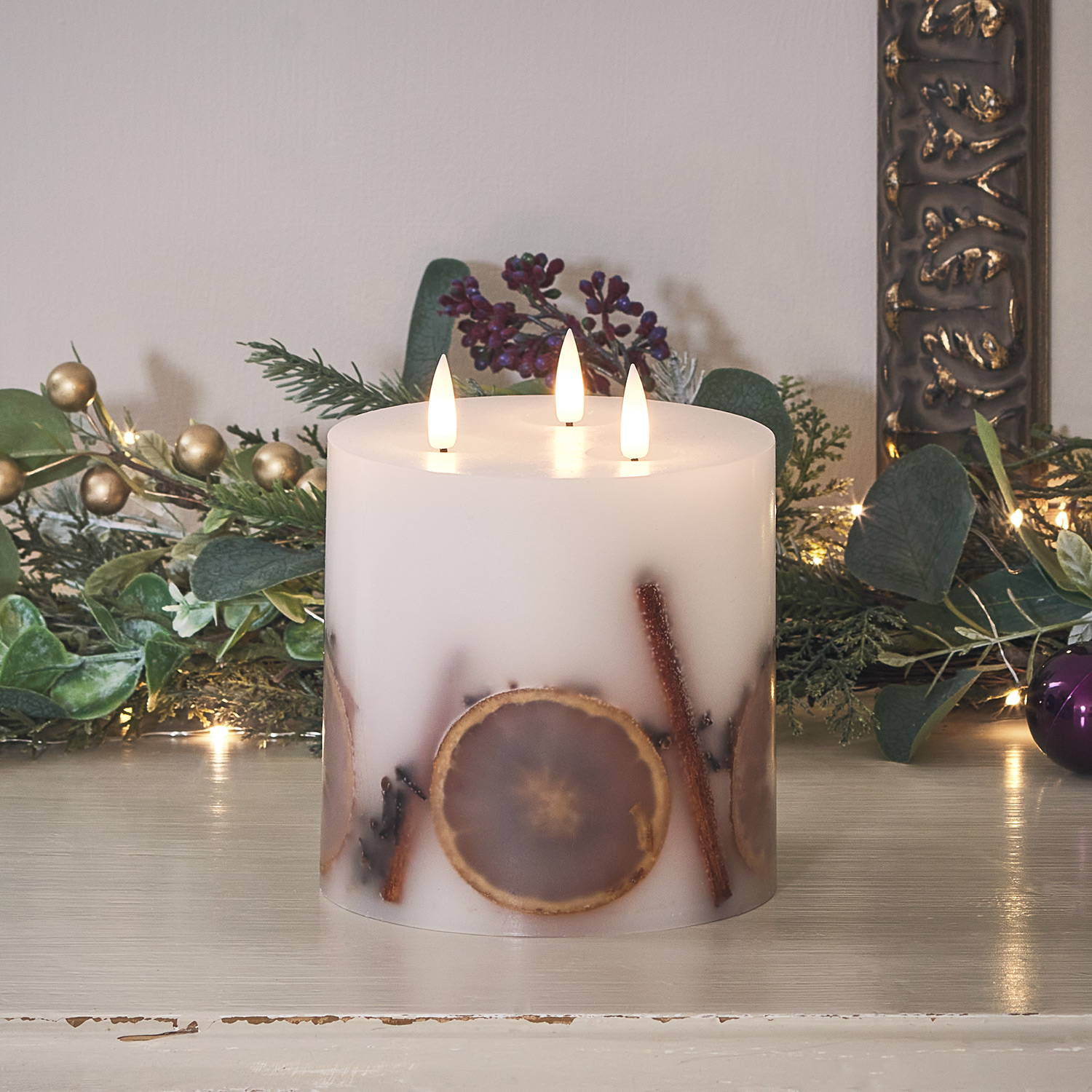 A three wick candle with encased sticks of cinnamon , dried orange and  berries