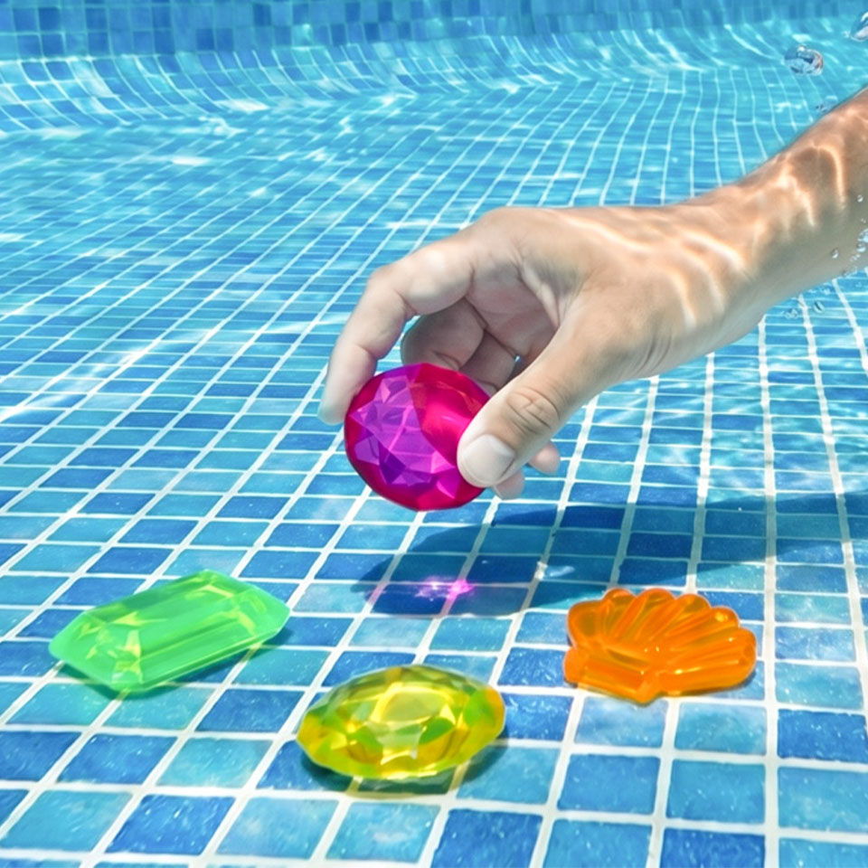 A hand reaching for colorful pool toys in a swimming pool.