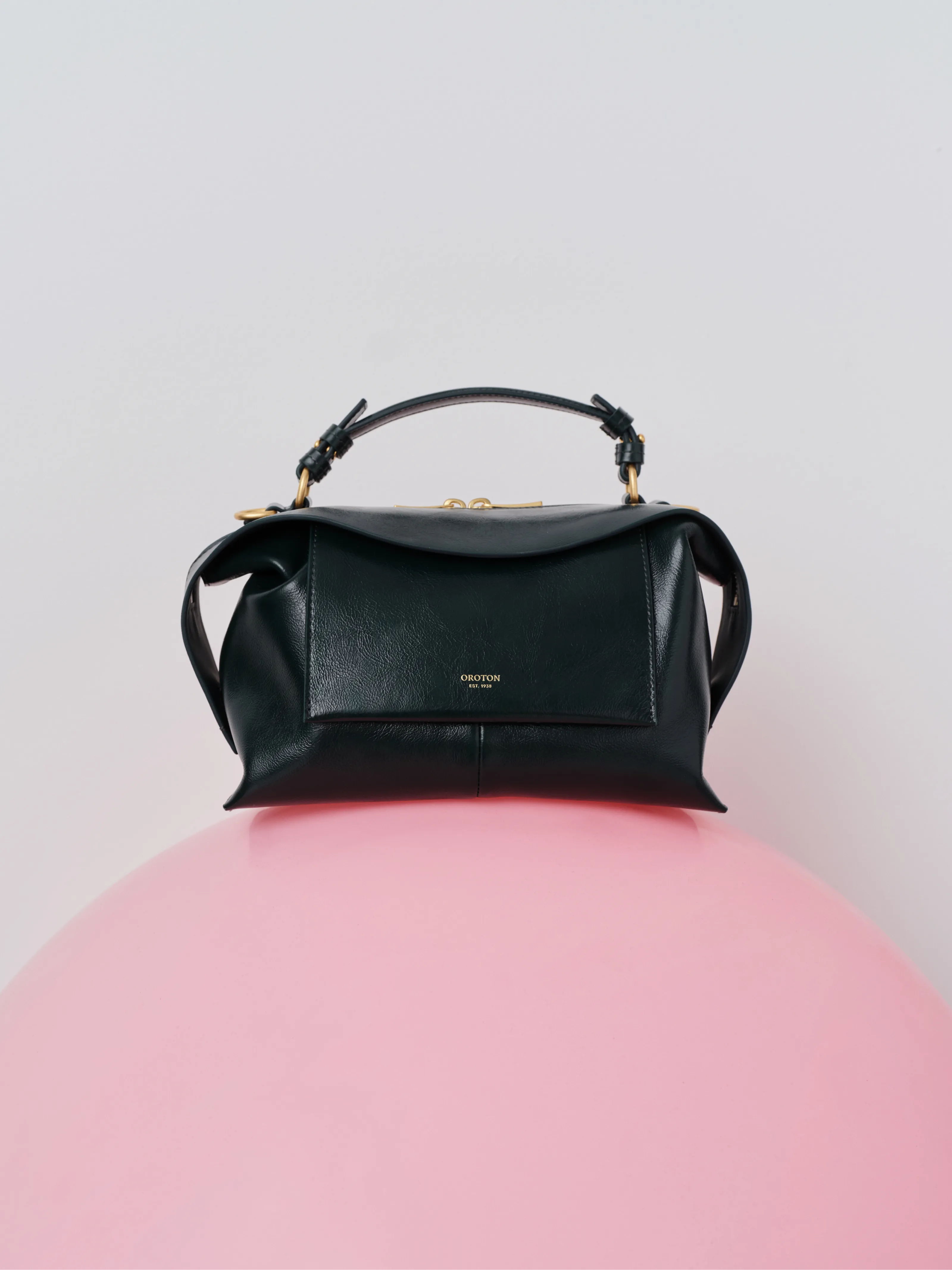 Black leather handbag resting on a pink round surface.