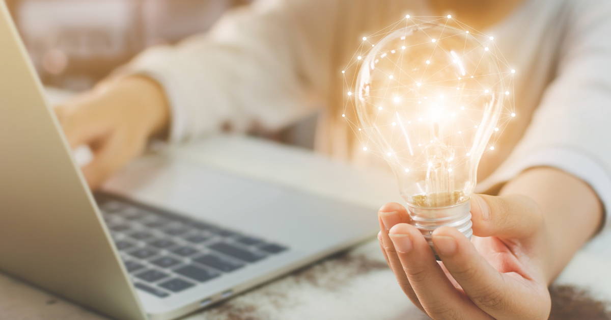 Hand holding a bright lightbulb while using a laptop