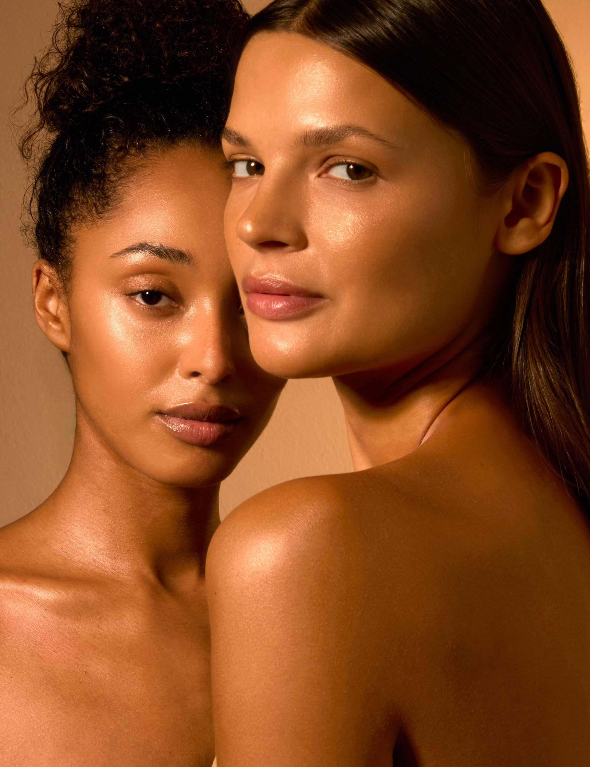 Two women with glowing skin, standing close together, facing the camera.