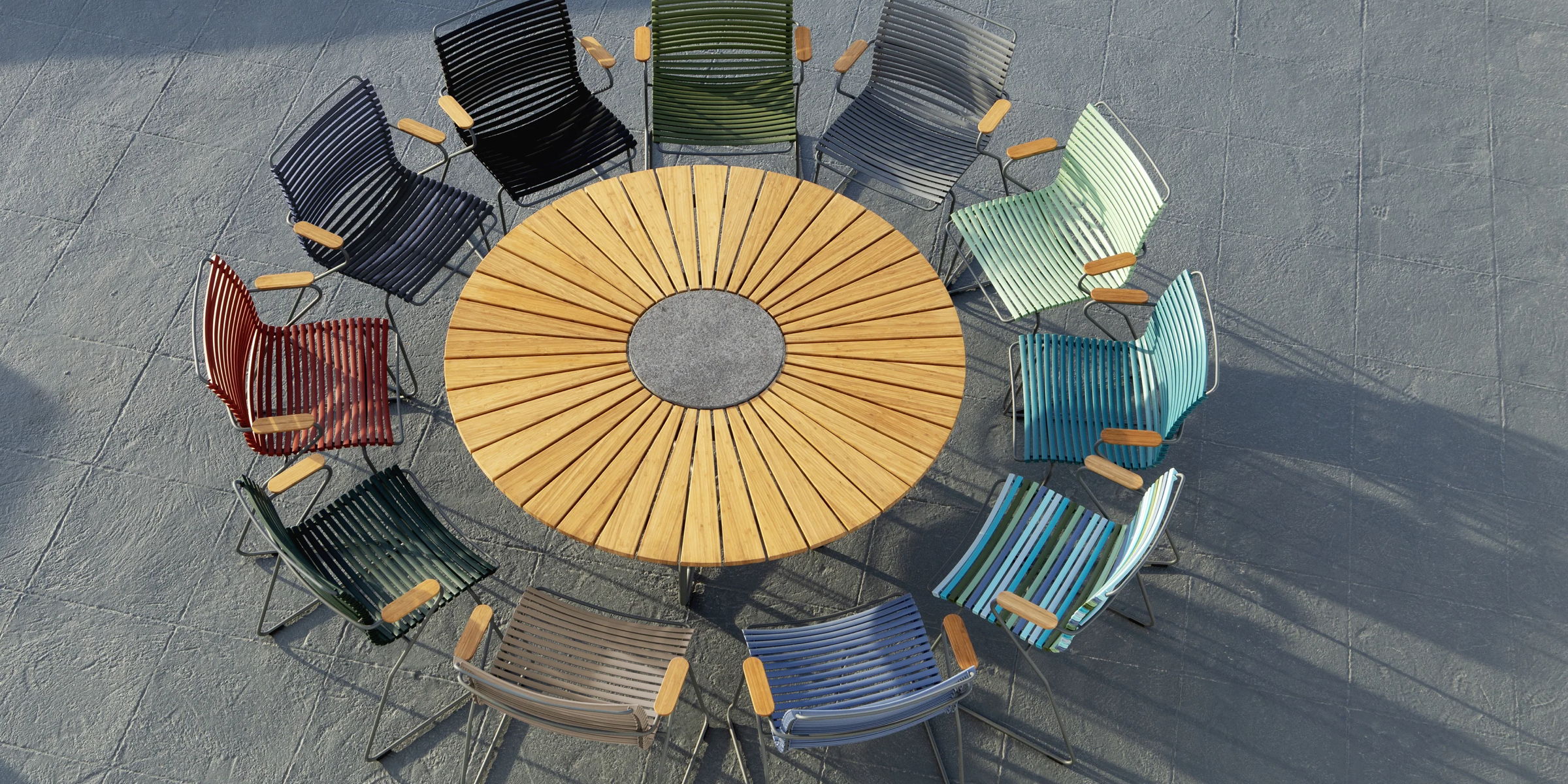 Overhead view of a round wood outdoor dining table surrounded by colorful modern dining chairs.