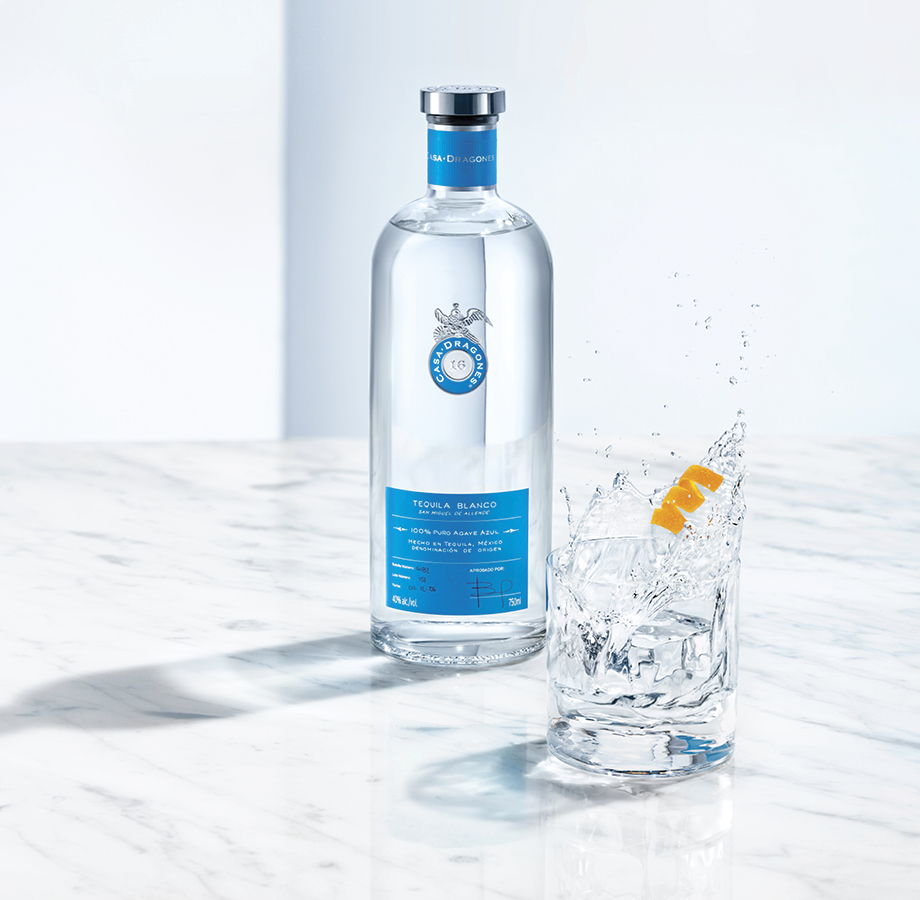 A bottle of clear liquid next to a glass with ice and an orange slice.