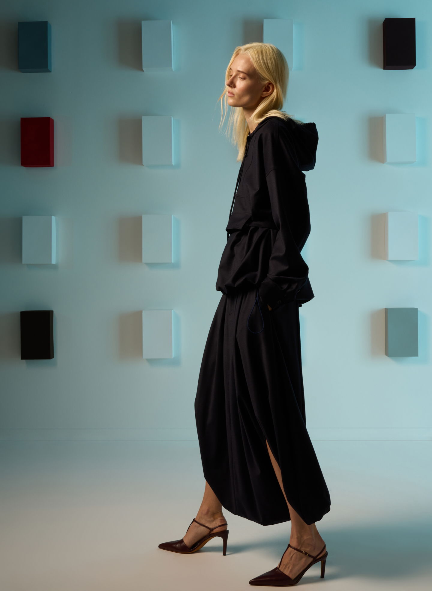 Model in black outfit walking against a colorful backdrop.