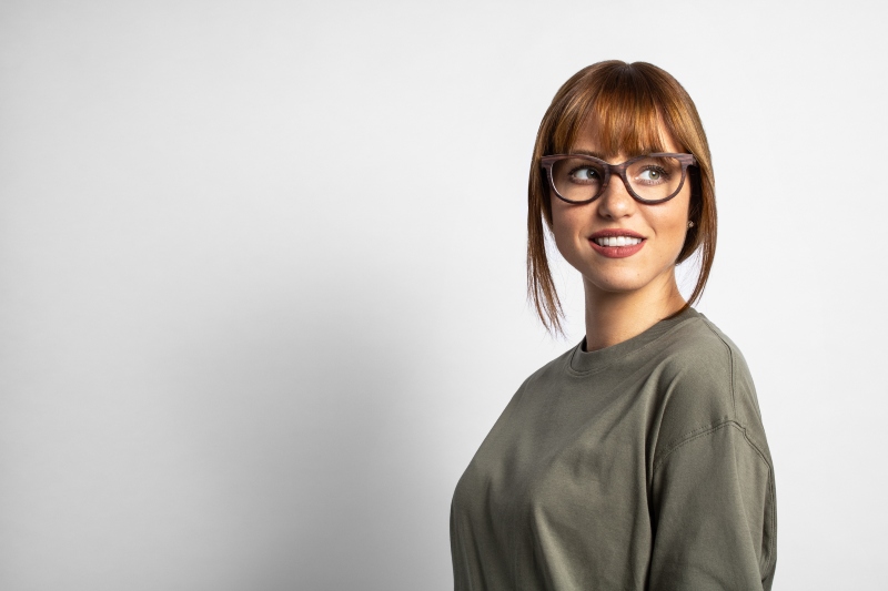 woman with round face wearing Charm Purple, cat-eye glasses frames, on a grey background