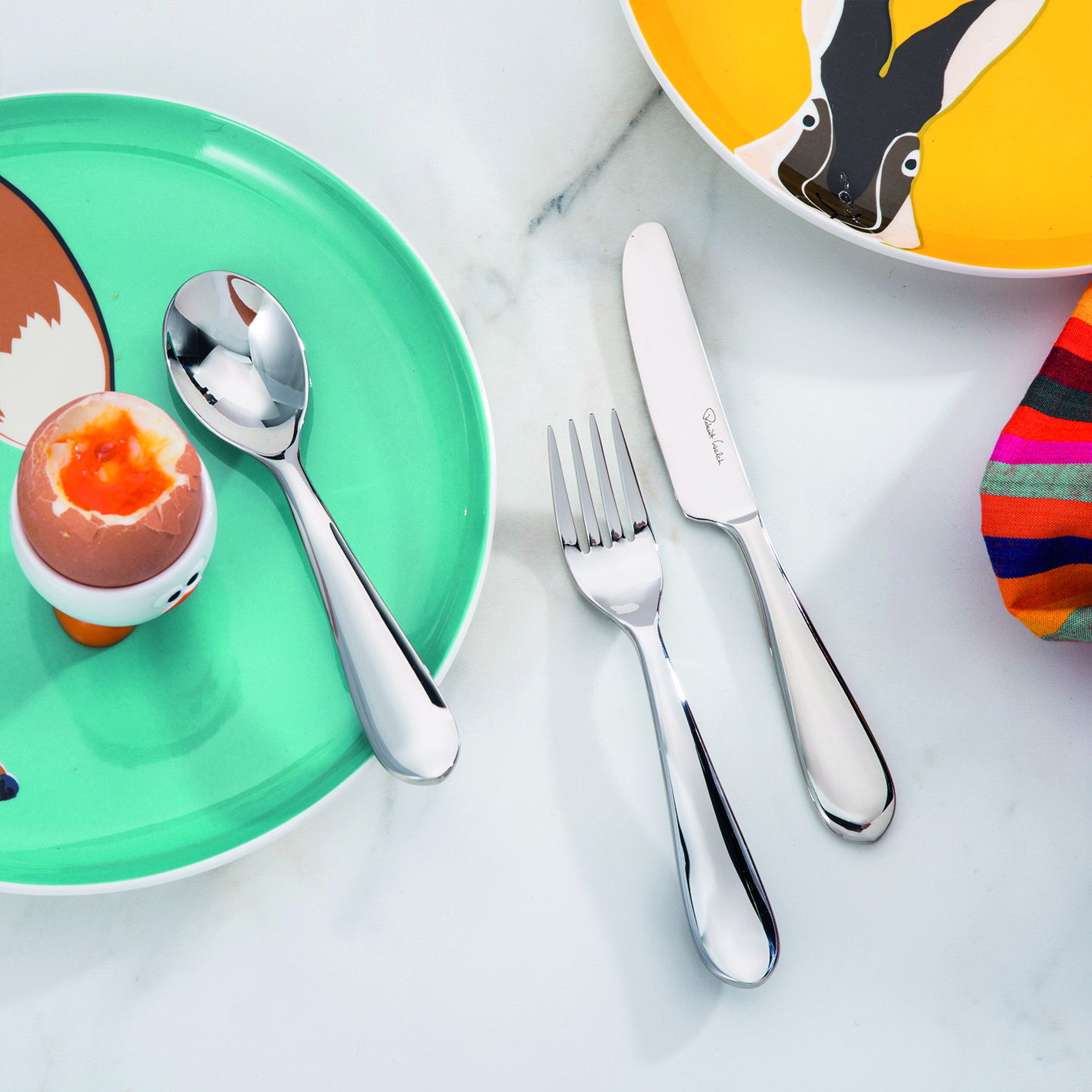 Colorful plates and Norton Bright Children's Cutlery arranged on a table.