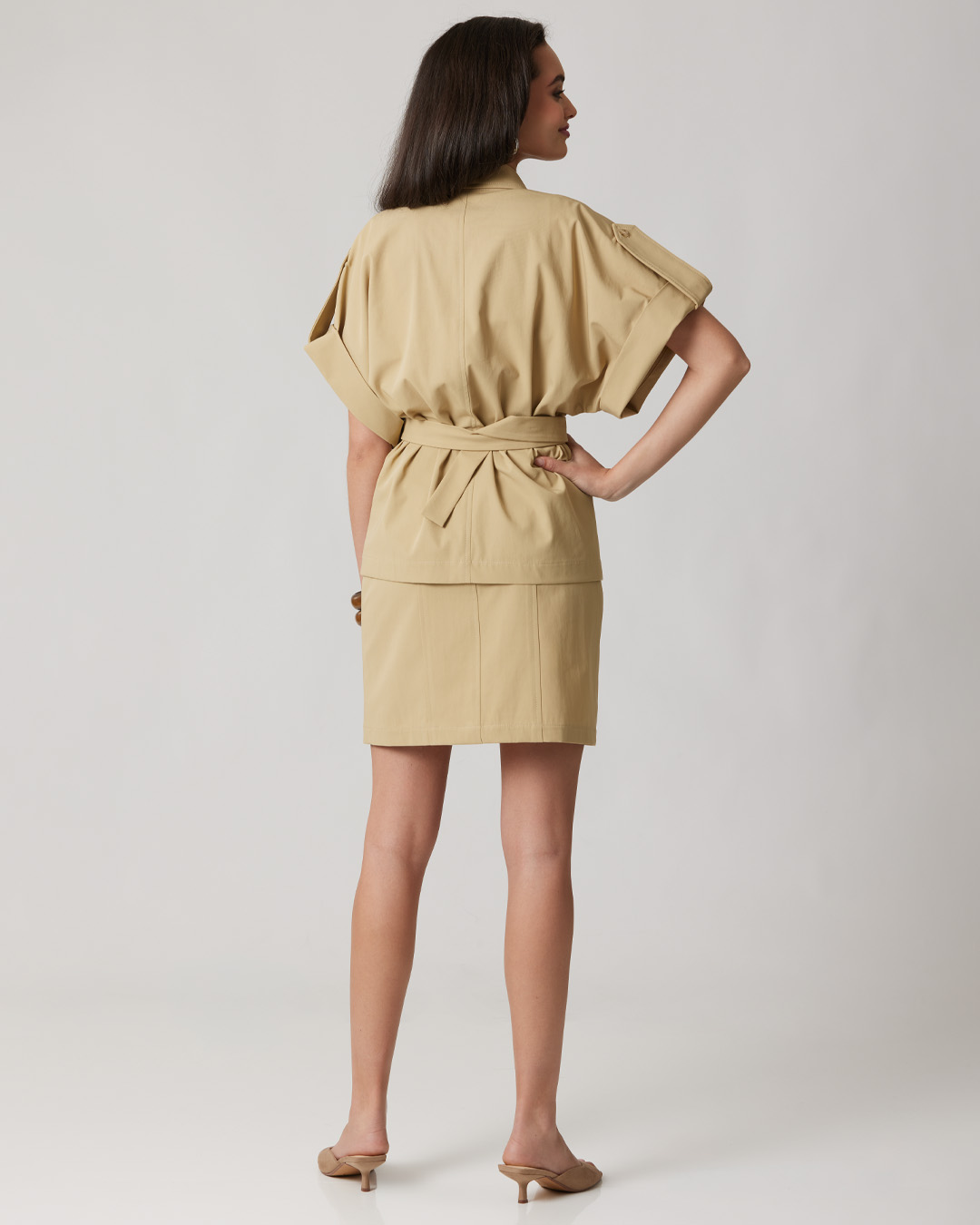 Woman in a white top and beige skirt, posing confidently.