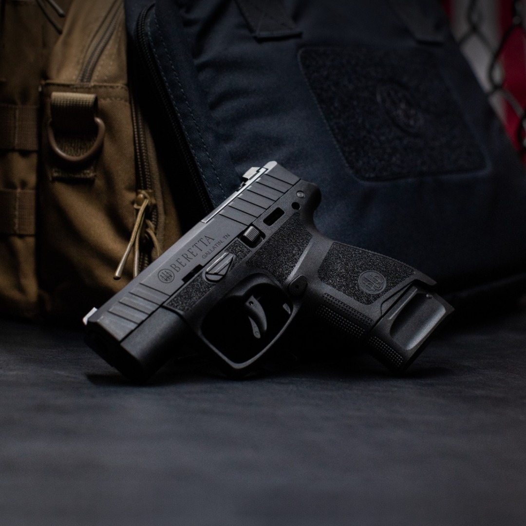 A black handgun resting on a dark surface near bags.
